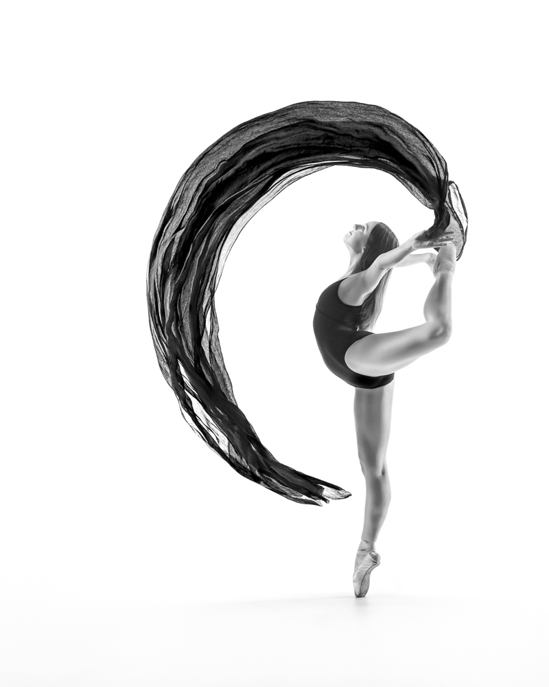 Ballerina in big attitude on pointe with flowing fabric.