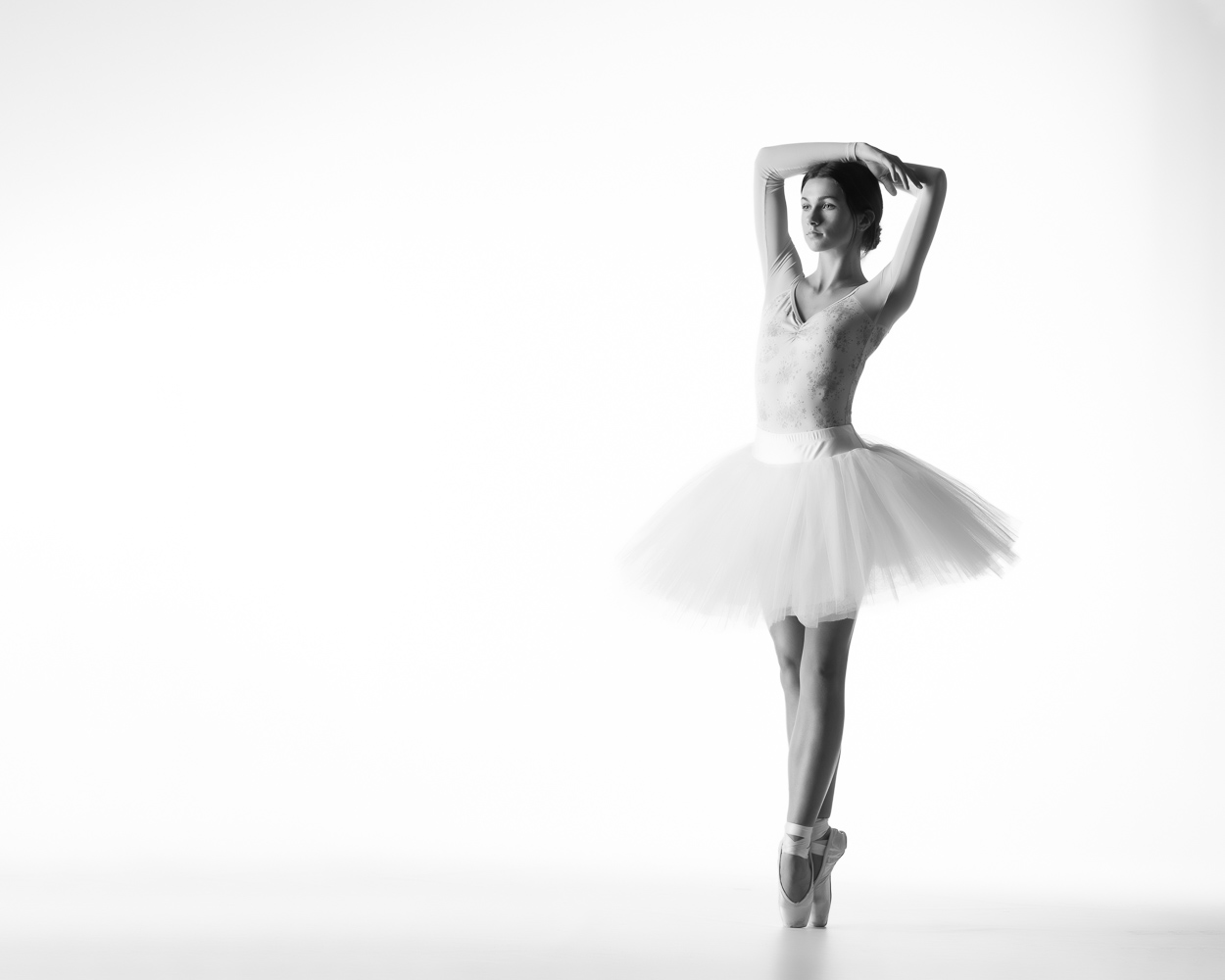 Ballerina all in white on white background in pensive fifth