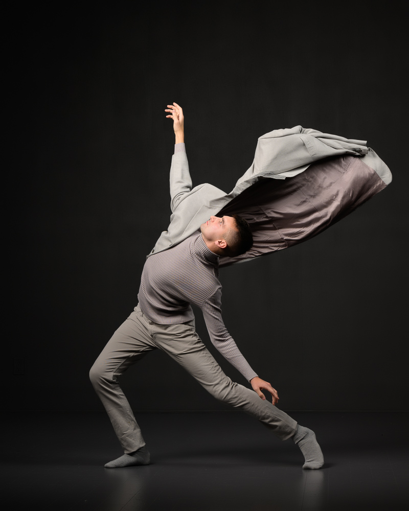 Contemporary male dancer all in grey with jacket flying away off one arm.