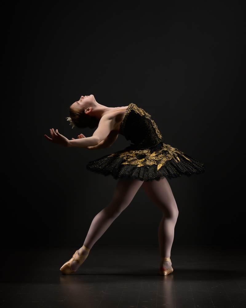 Teen ballerina in black swan tutu in 4th cambre.