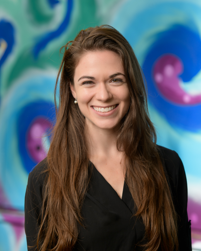 Dance Headshot of woman with long brown hair and big smile against a colorful mural.