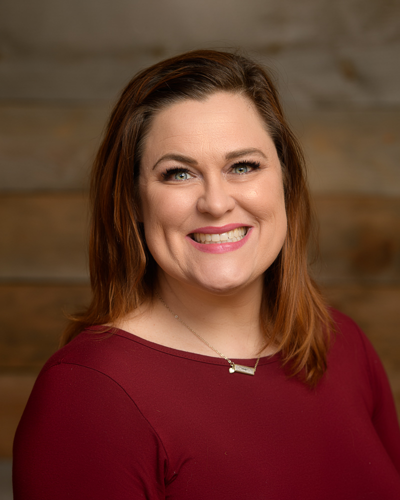 Professional Headshot of a woman with a big smile. Background is a barnwood wall.