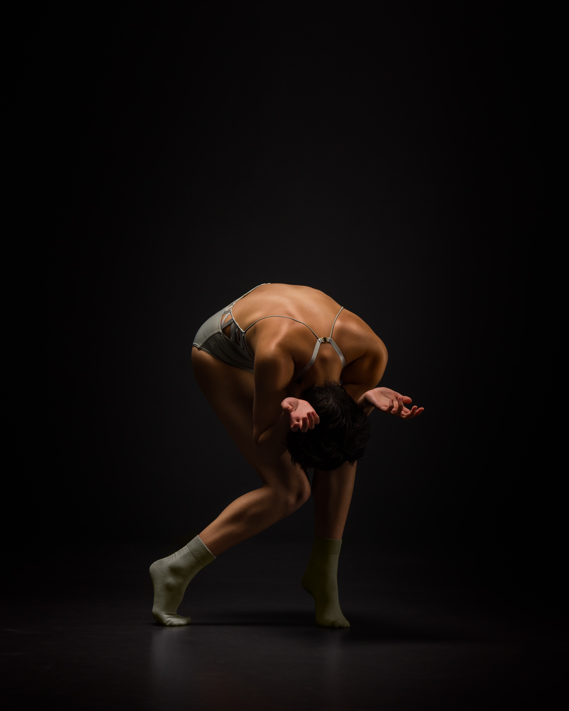 A contemporary dances in a tortured pose fully contracted with head bowed, and palms left turned upward.