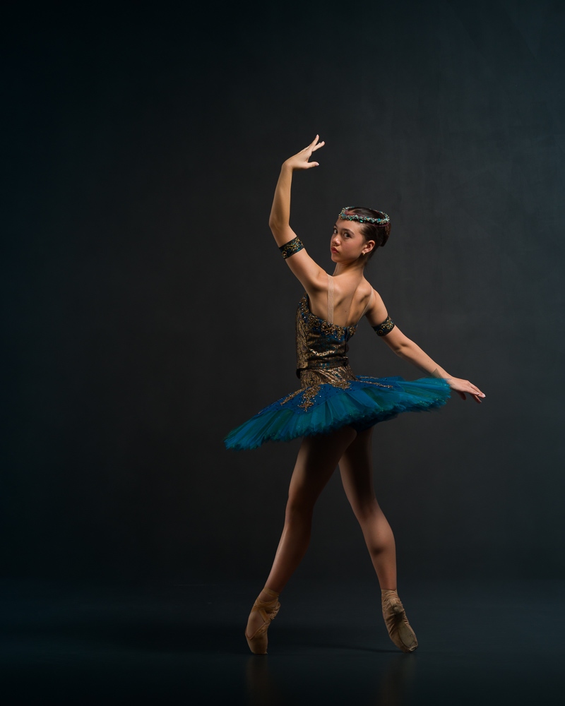 Dancer in blue and gold tutu in fourth position looking back to camera