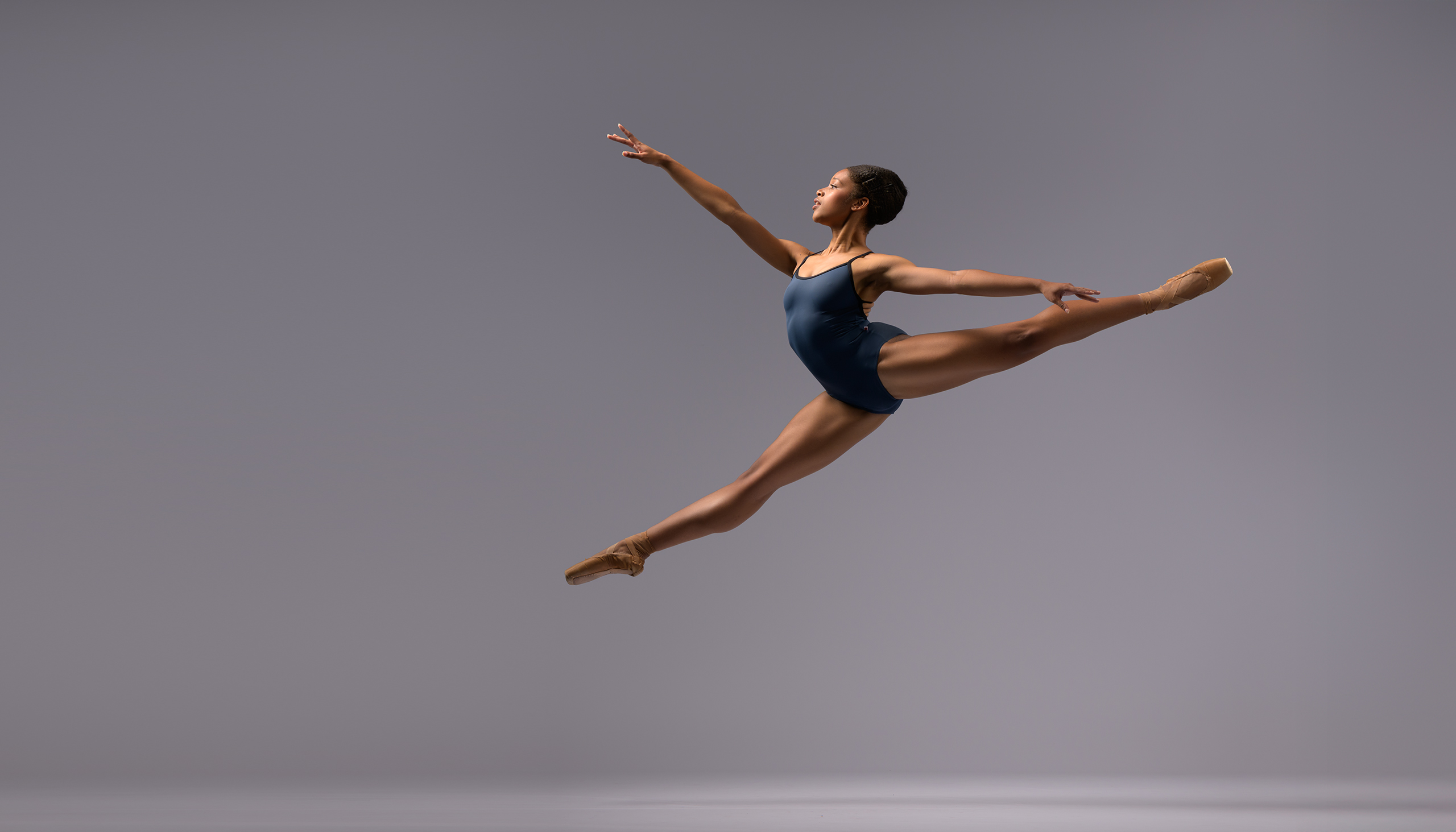 Ballerina in blue jumping a sissonne on a grey background for an audition photo