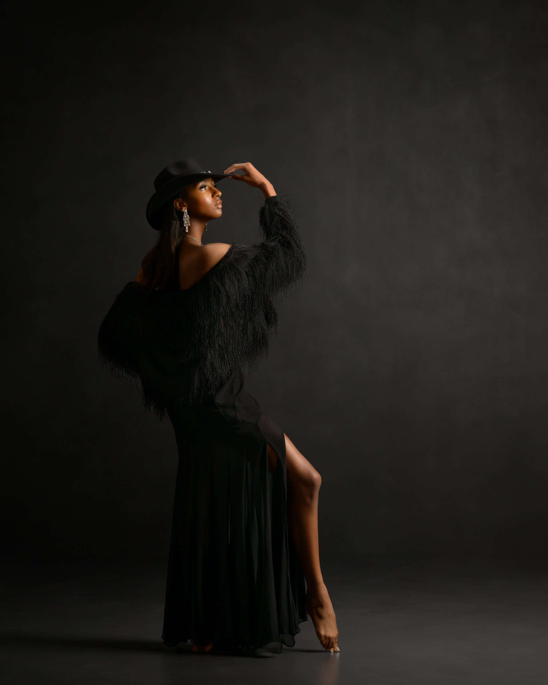Dancer in cowgirl hat and black fuzzy stole and long black skirt against dark background. Only leading lines are lit.