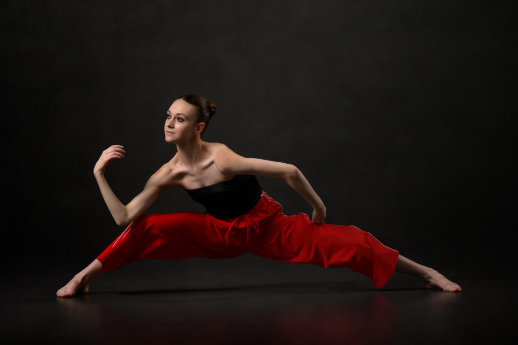 Contemporary Dancer in low wide lunge in red pants with a twisted arm line and forward lean