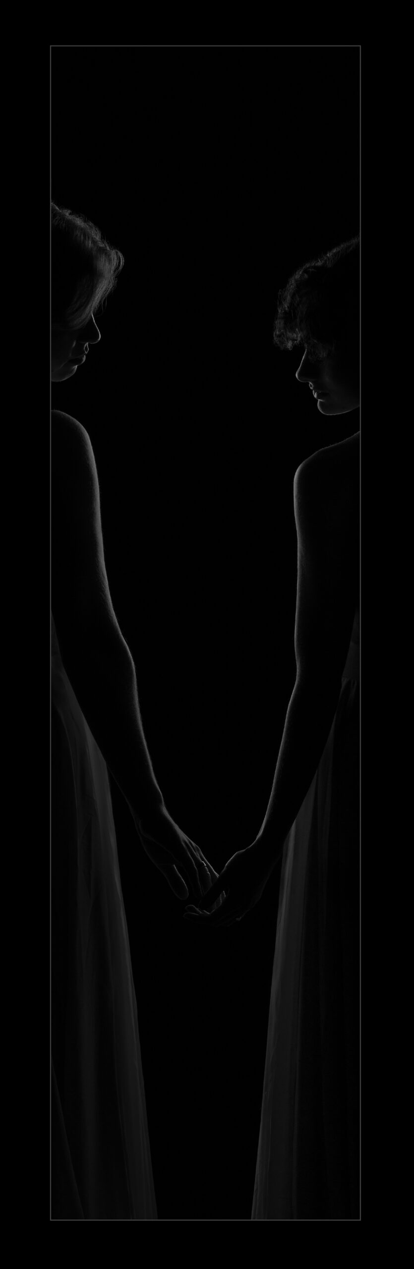 Two women barely touching hands rim-lit in a narrow opening.