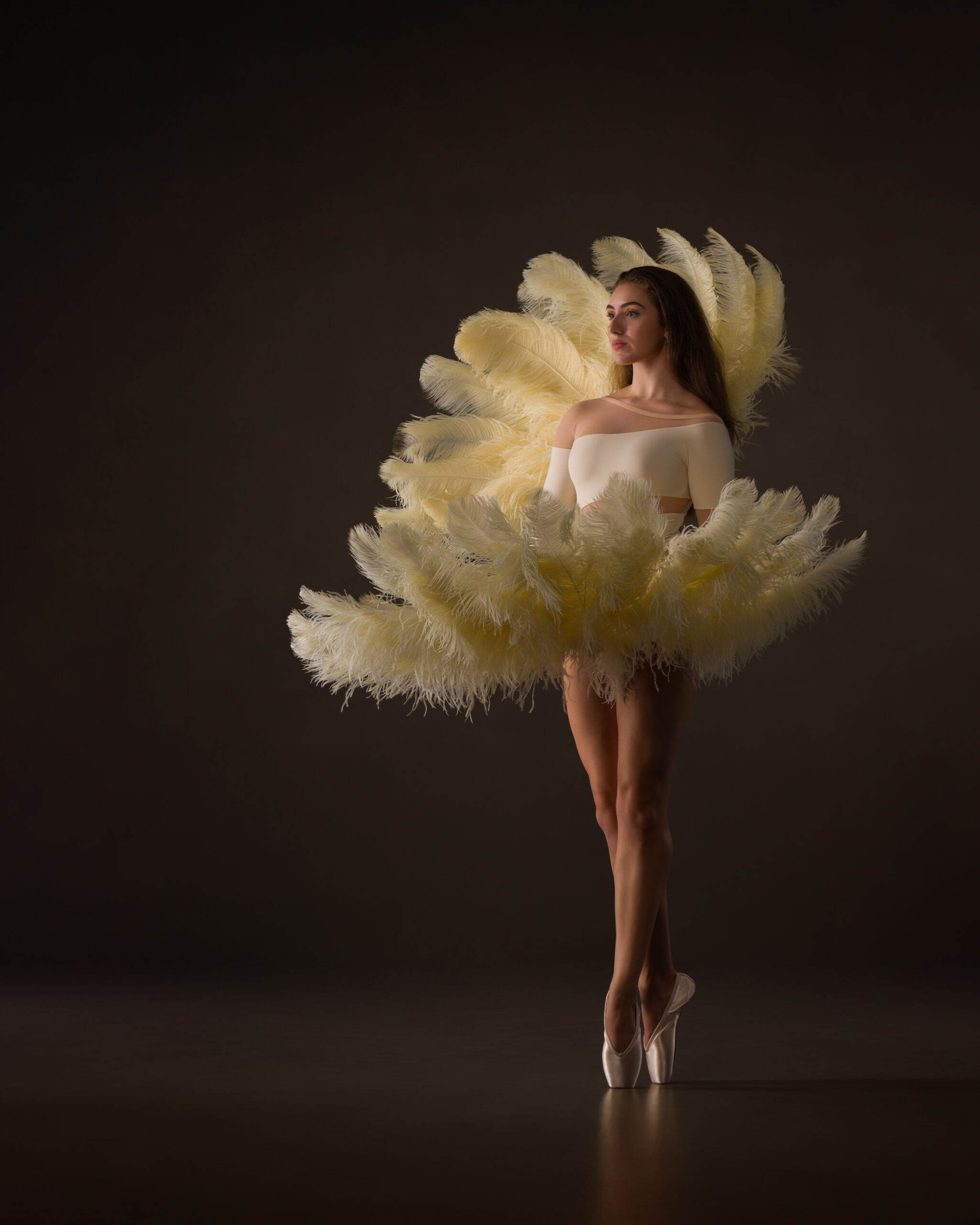 Teen dancer as if emerging from a clamshell formed of feather fans.