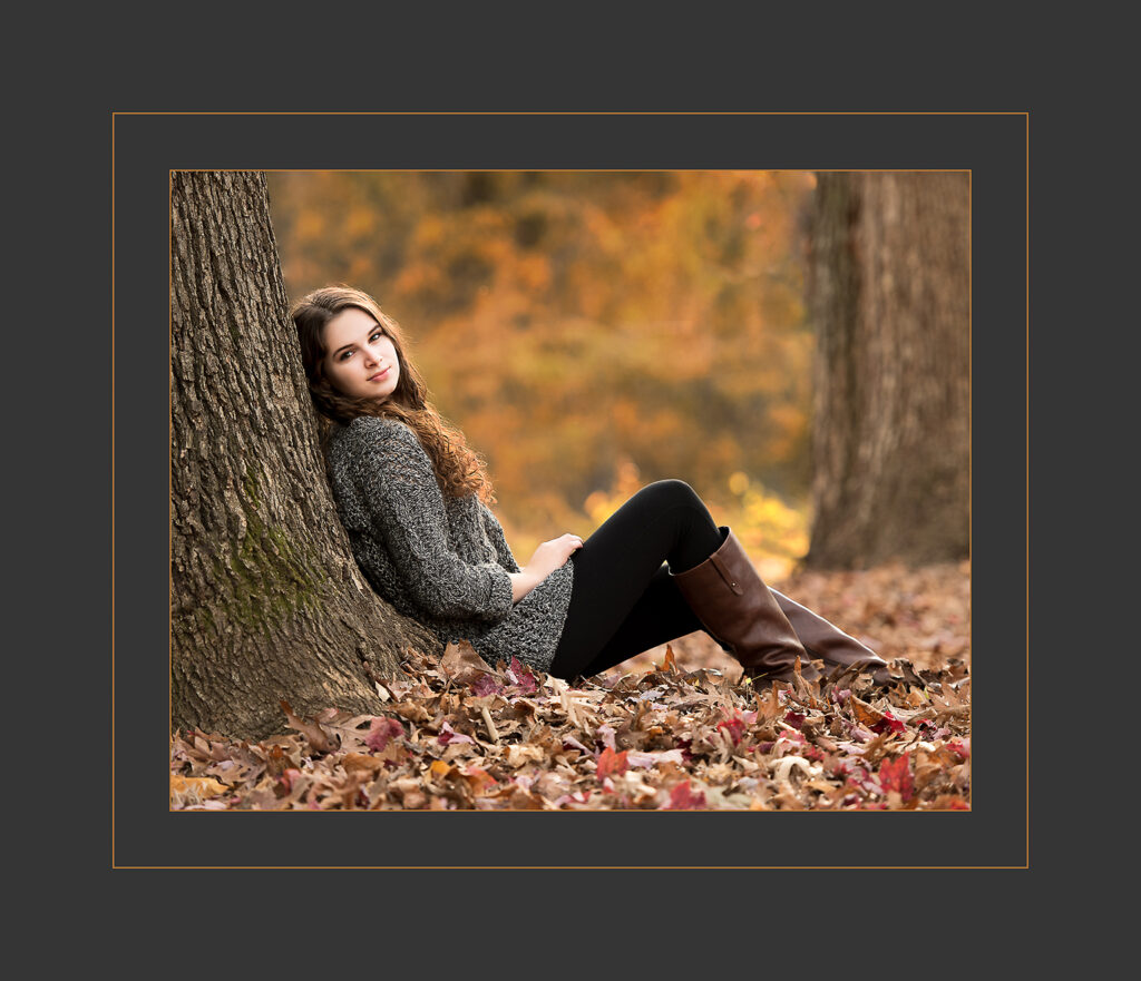 Young woman sitting under a tree surrounded by fall color.